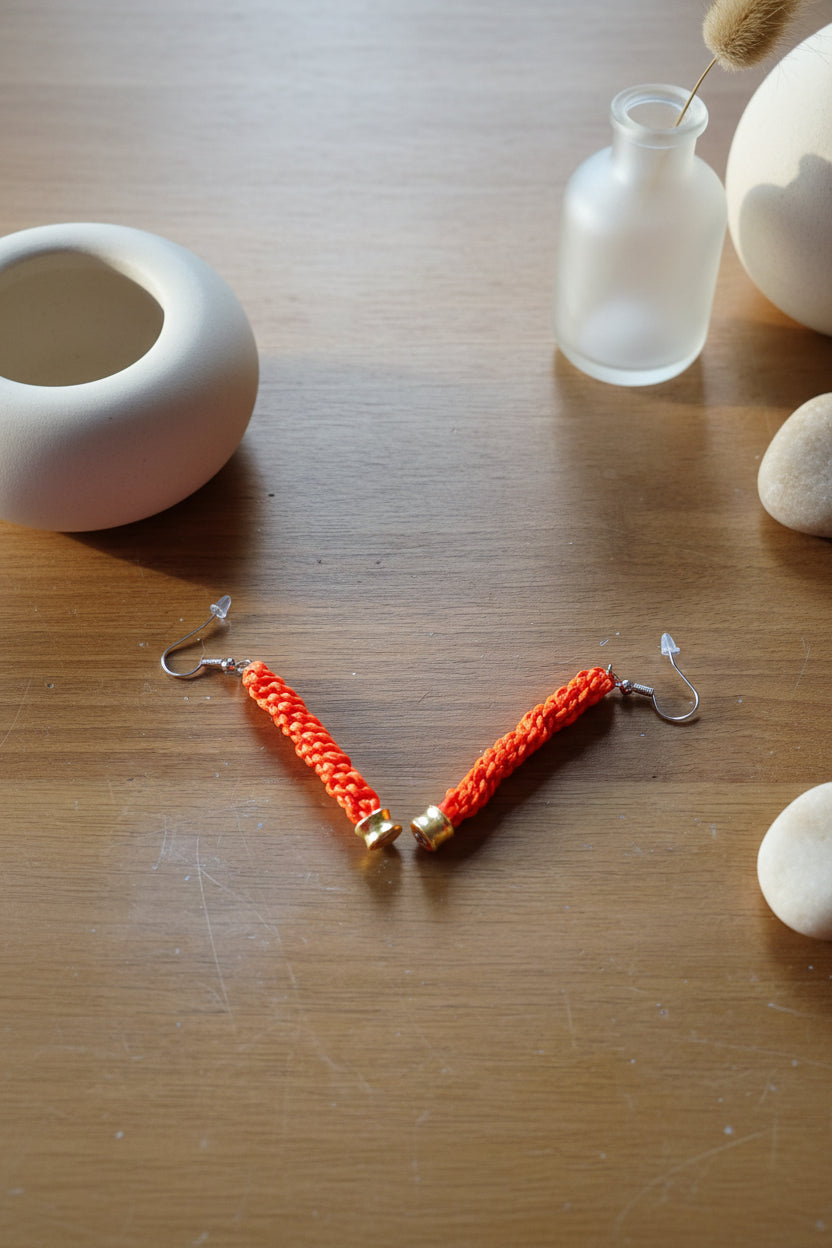 Dettaglio degli orecchini pendenti in Microparacord arancione con monachelle in acciaio inox