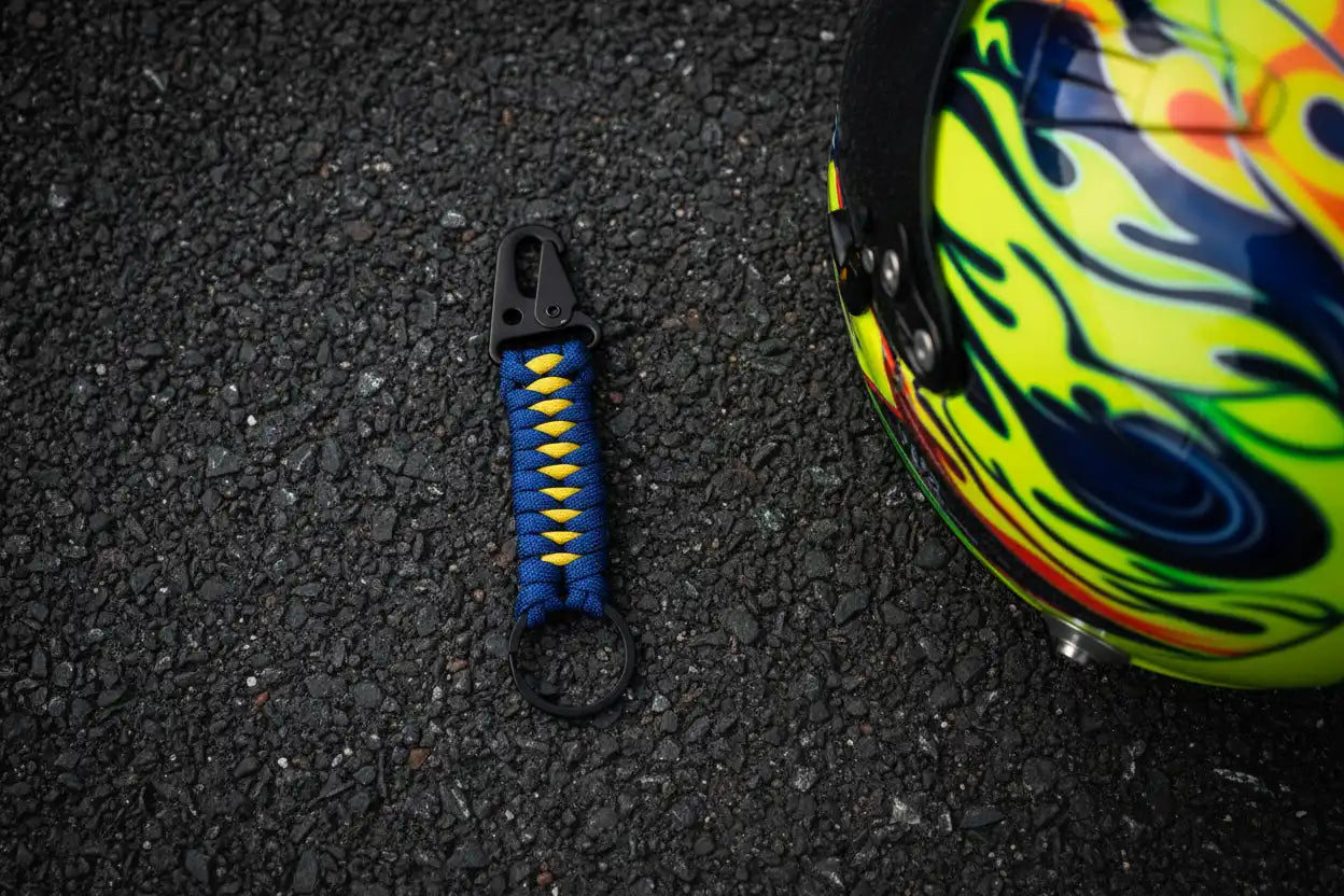 Portachiavi Dragon Key in Paracord blu e giallo con casco da pilota su asfalto